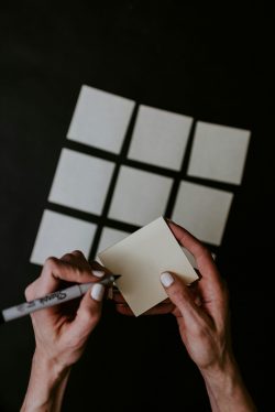 Postits on a dark background, hands writing on one