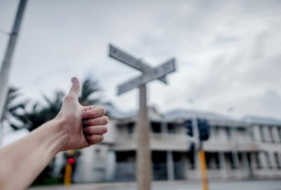 Fokussierter Daumen hoch vor einem Kreuzungs-Straßenschild im Hintergrund (Daumenregel)